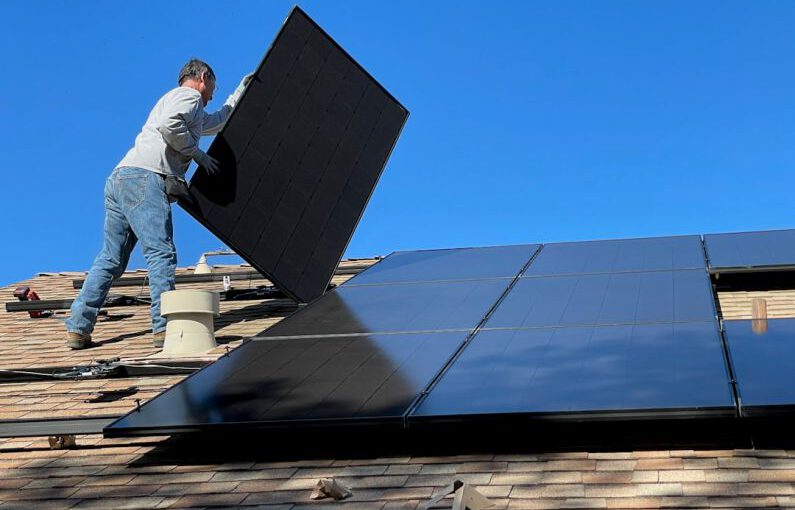Solar Panels Roof - man in white dress shirt and blue denim jeans sitting on white and black solar panel
