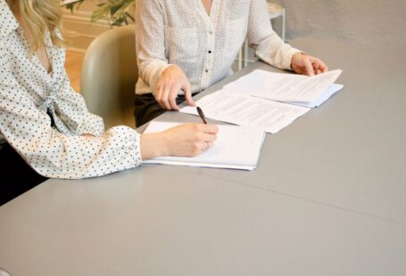 Tax Credit Document - woman signing on white printer paper beside woman about to touch the documents